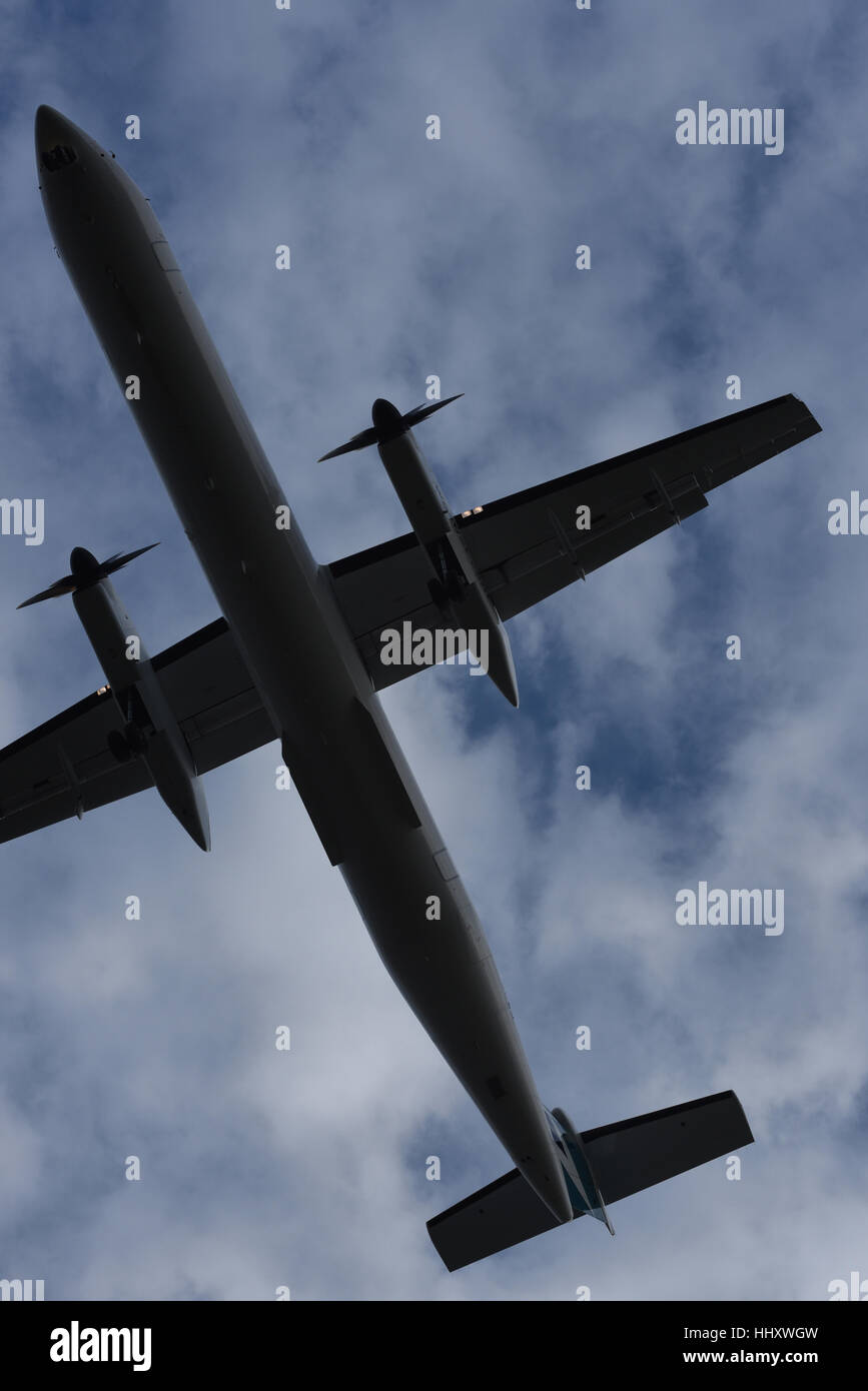 Partial view of the undercarriage of a propellor driven aircraft coming in for a landing beneath a clouded sky Stock Photo