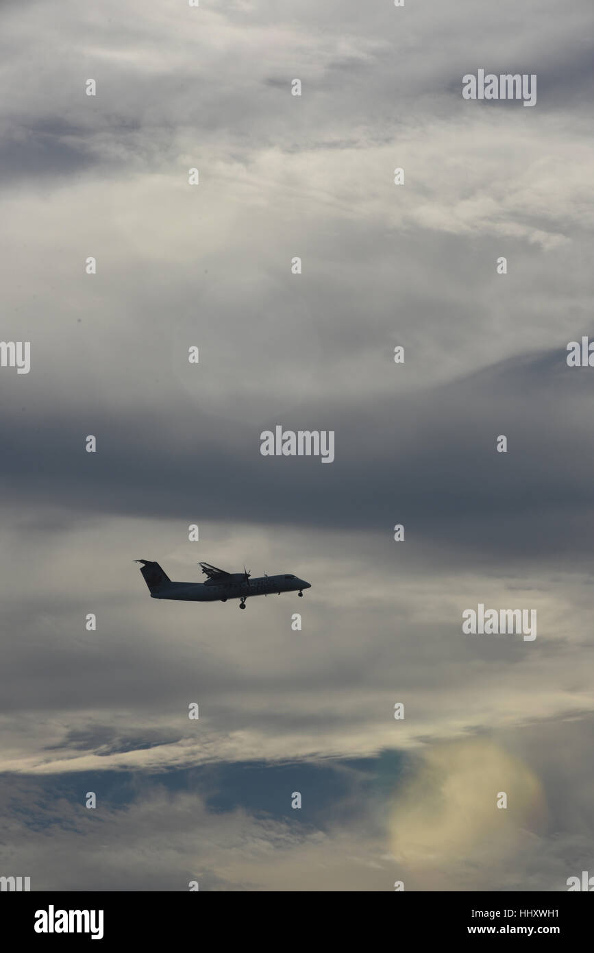 A small commercial aircraft is silhouetted against a cloudy sky as it comes in for an airport landing Stock Photo