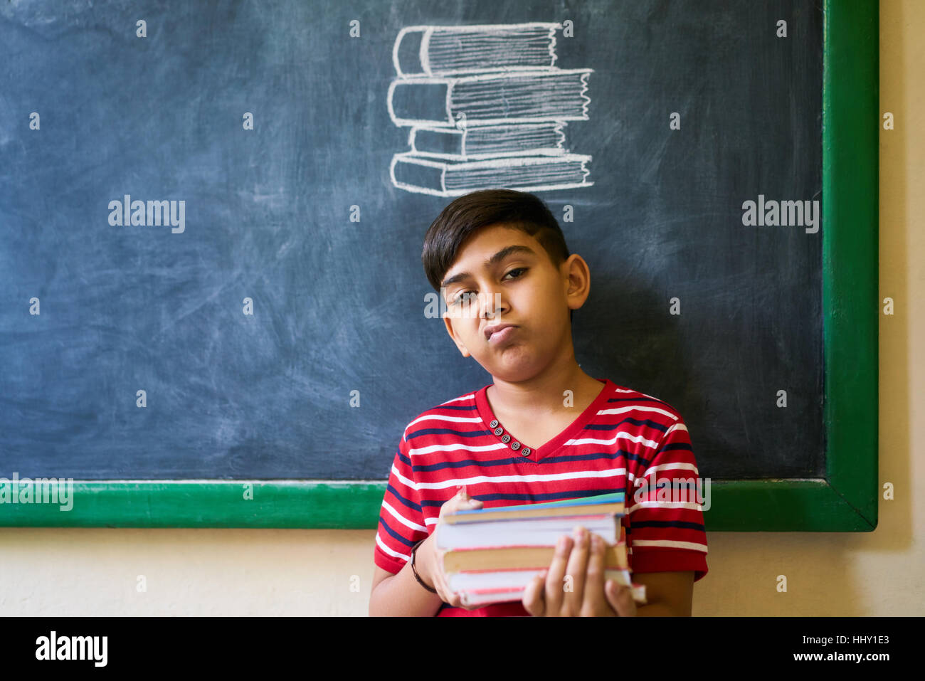 Concept on blackboard at school. Young people, student and pupil in classroom. Sad and bored hispanic boy in class. Portrait of male child looking at Stock Photo