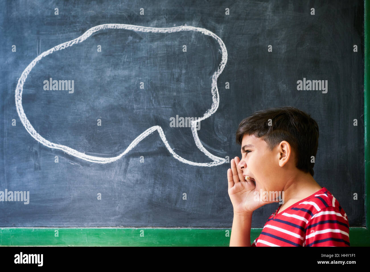 Concept on blackboard at school. Young people, student and pupil in classroom. Hispanic boy screaming in class with drawing of cloud on blackboard. Po Stock Photo