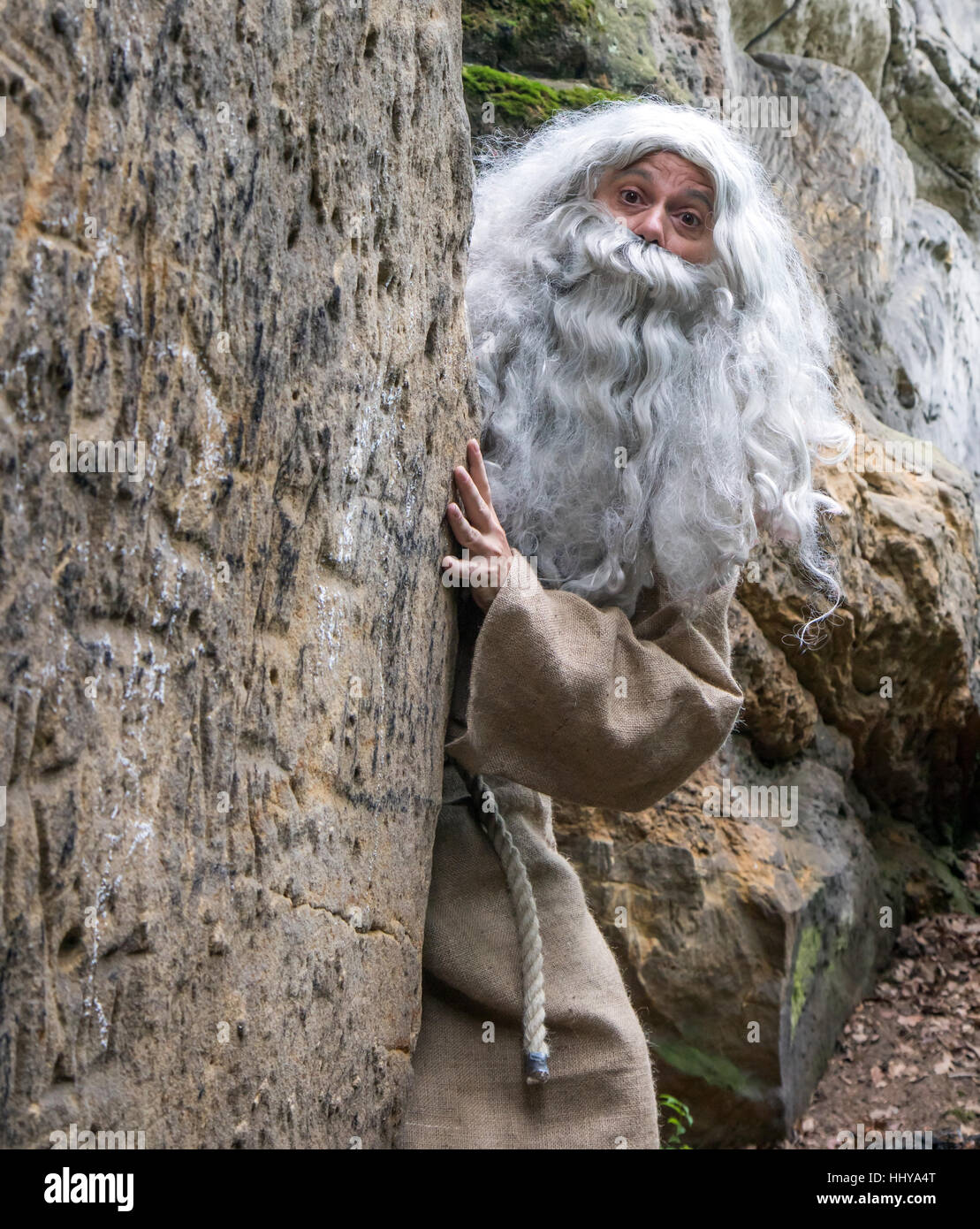 Surprised hermit peeks behind rock. The bearded monk in nature. Stock Photo