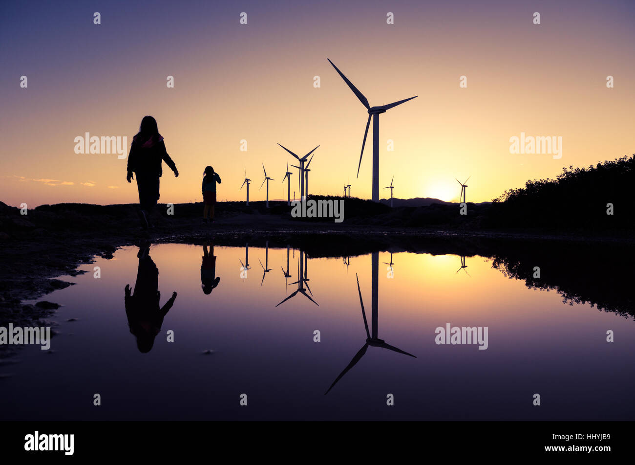 Wind turbines at a wind farm with the silhouettes of two girls ...