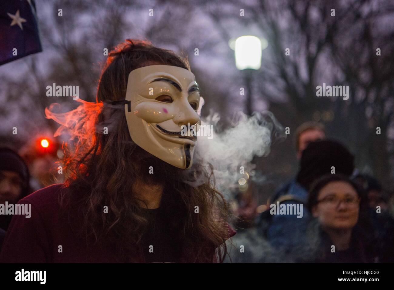 Protestors at the inauguration of President Donald Trump in Washington, D.C. A young Caucasian man wearing a Guy Fawkes mask exhales e-cigarette vapors, as he participates in protest activities in a park. Stock Photo