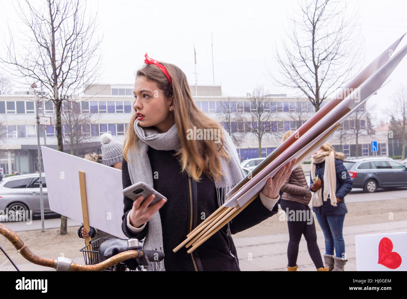 Woman on bicycle distributes placards in front of the US Embassy in Copenhagen. She takes part in womens march, a worldwide protest against Donald Trump on January 21, 2017, Stock Photo