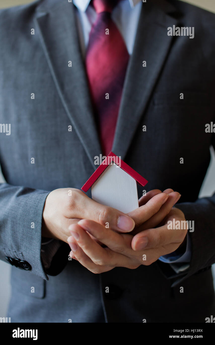 Business man in suit having miniature house on palm of his hand - Business mortgage, property loan, house insurance, business investment concept. Stock Photo