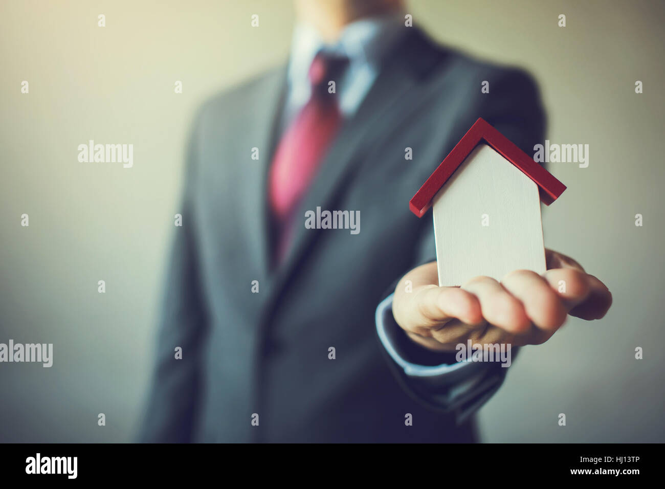 Business man in suit having miniature house on palm of his hand ...