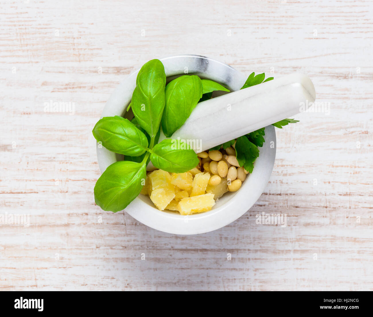 Top View of Green Fresh Basil Herbs in Pestle and Mortar with Parmesan cheese and Pine Nuts Stock Photo
