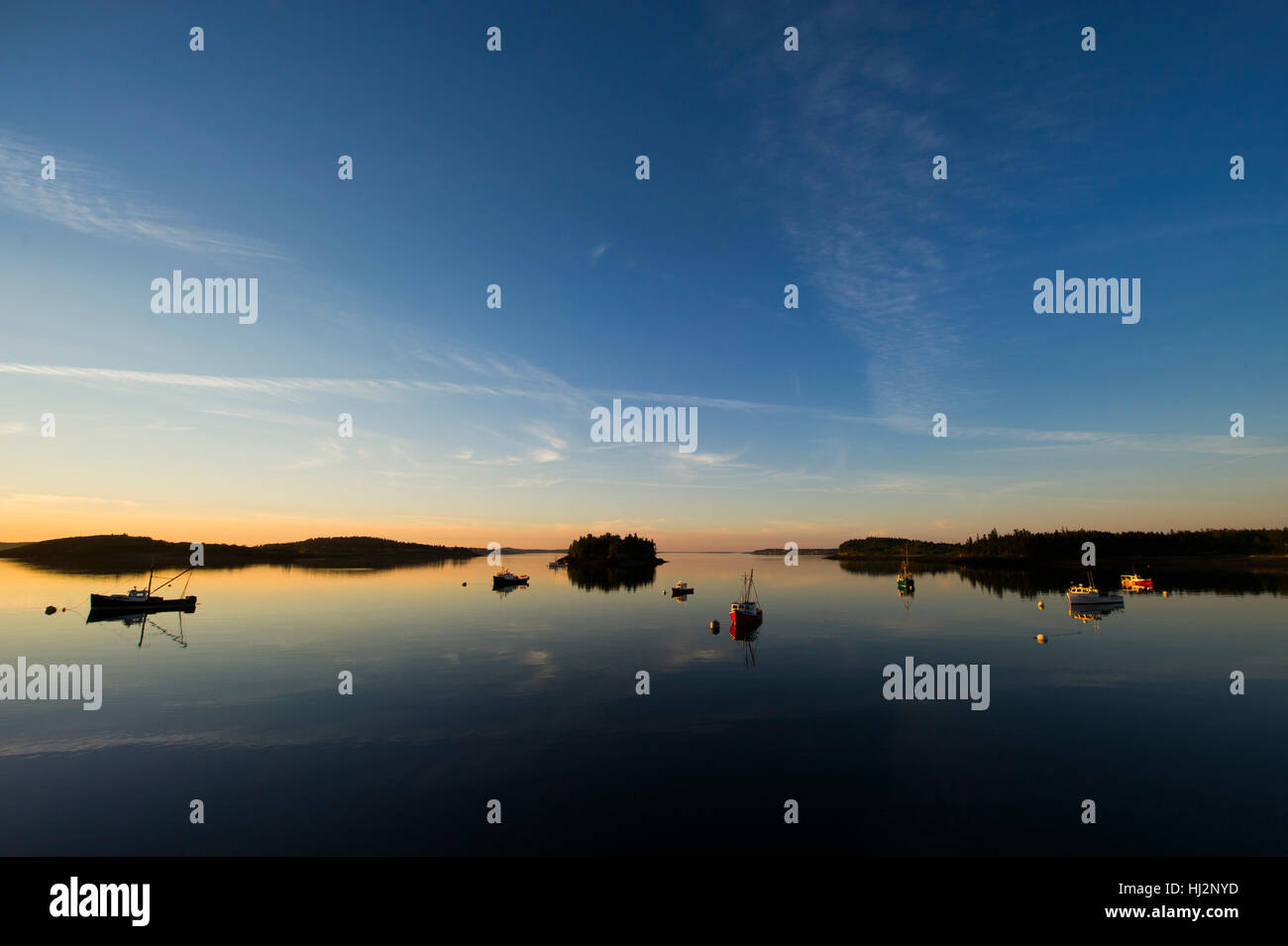 The sun sets over a calm harbor with many fishing boats anchored Stock ...