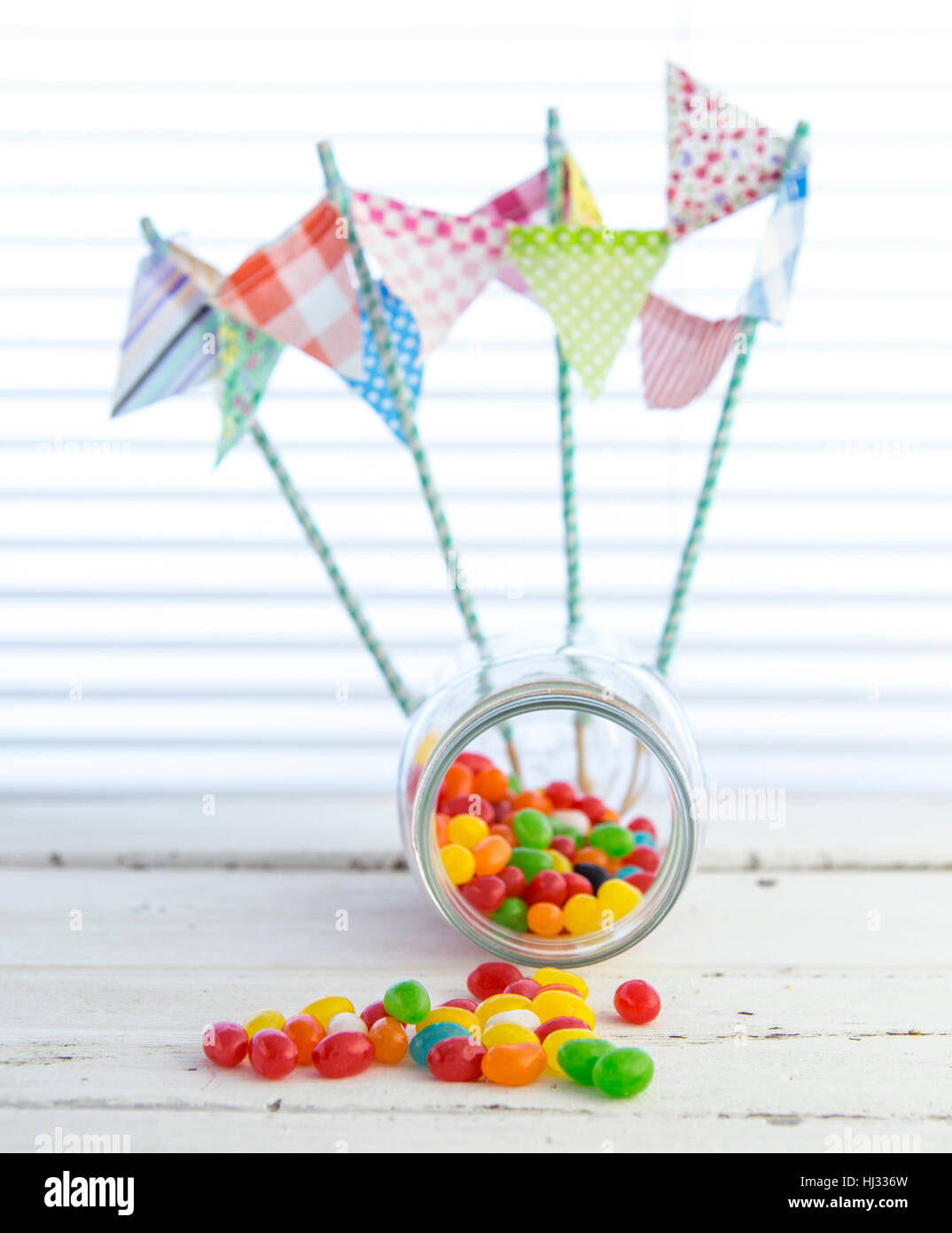 Colorful jellybeans spilling from a Jar with white rustic background Stock Photo