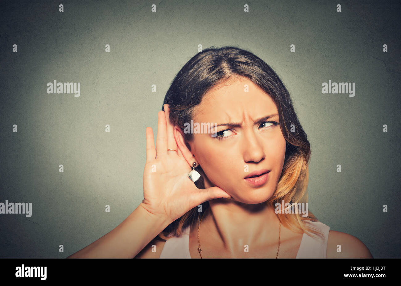 Closeup portrait concerned young nosy woman hand to ear gesture carefully intently secretly listening juicy gossip conversation news isolated grey bac Stock Photo