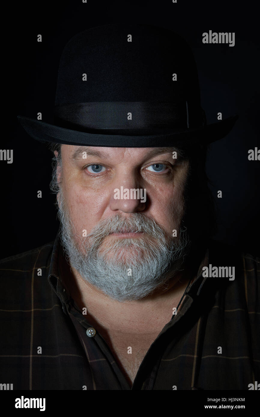 Portrait of the man with gray beard in black hat on the black background Stock Photo