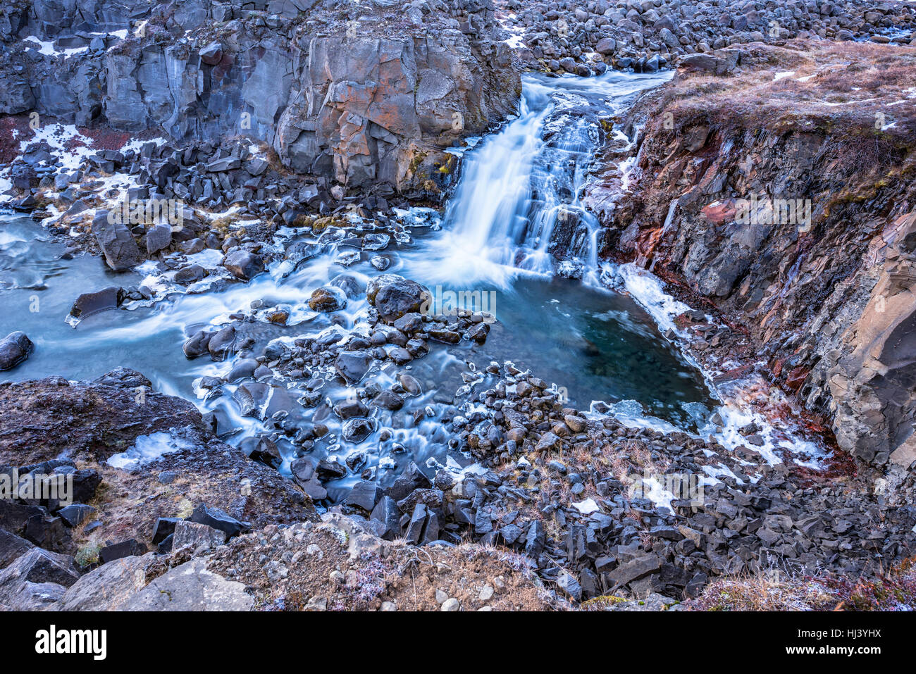 A waterfall in Iceland cascades down the side of a rugged mountain into a natural pool Stock Photo