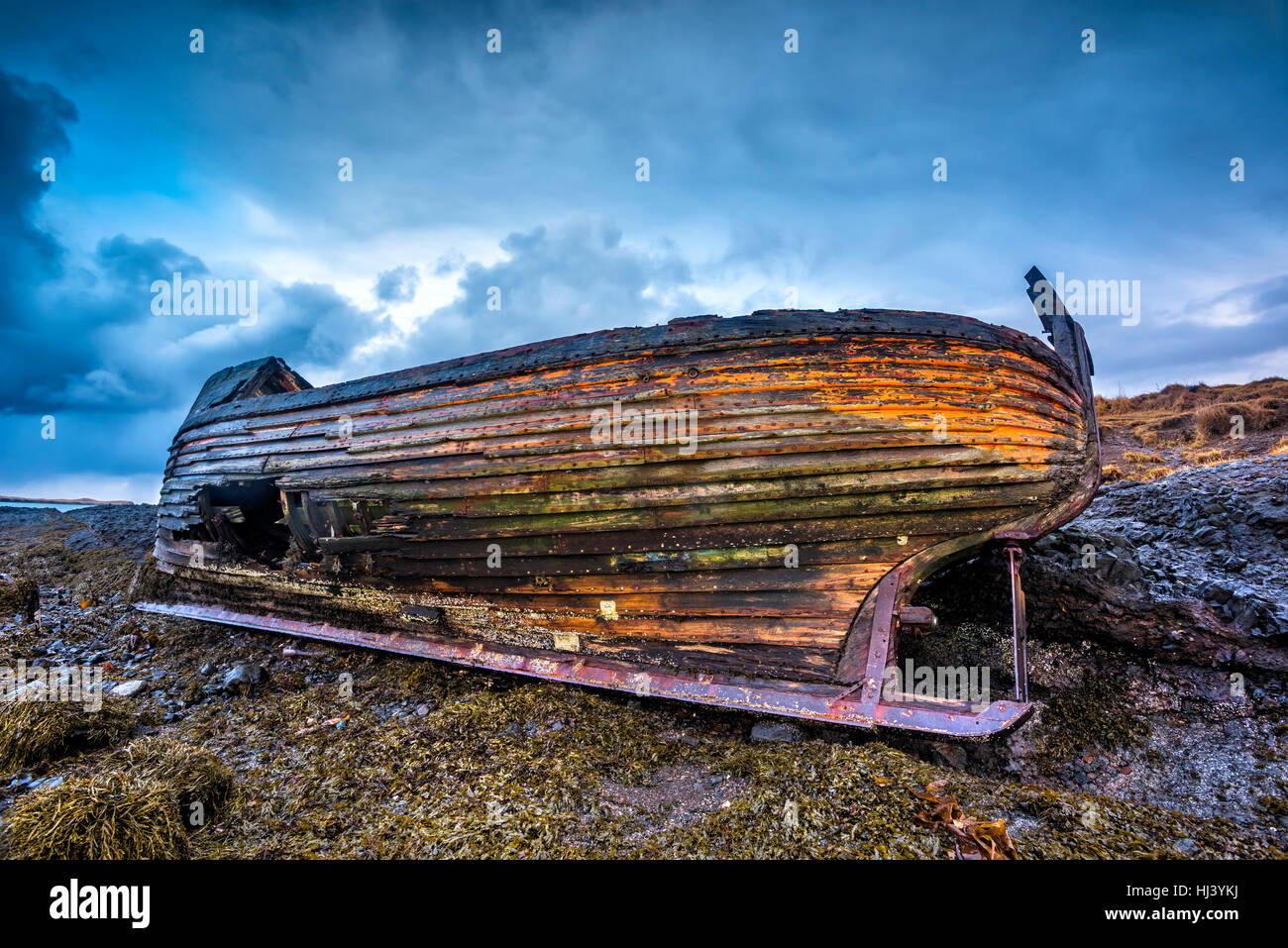 An old abandoned fishing vessel from the early 1900's rests on a remote beach as it rots, exposing the ship's wooden ribs and hull infrastructure. Stock Photo