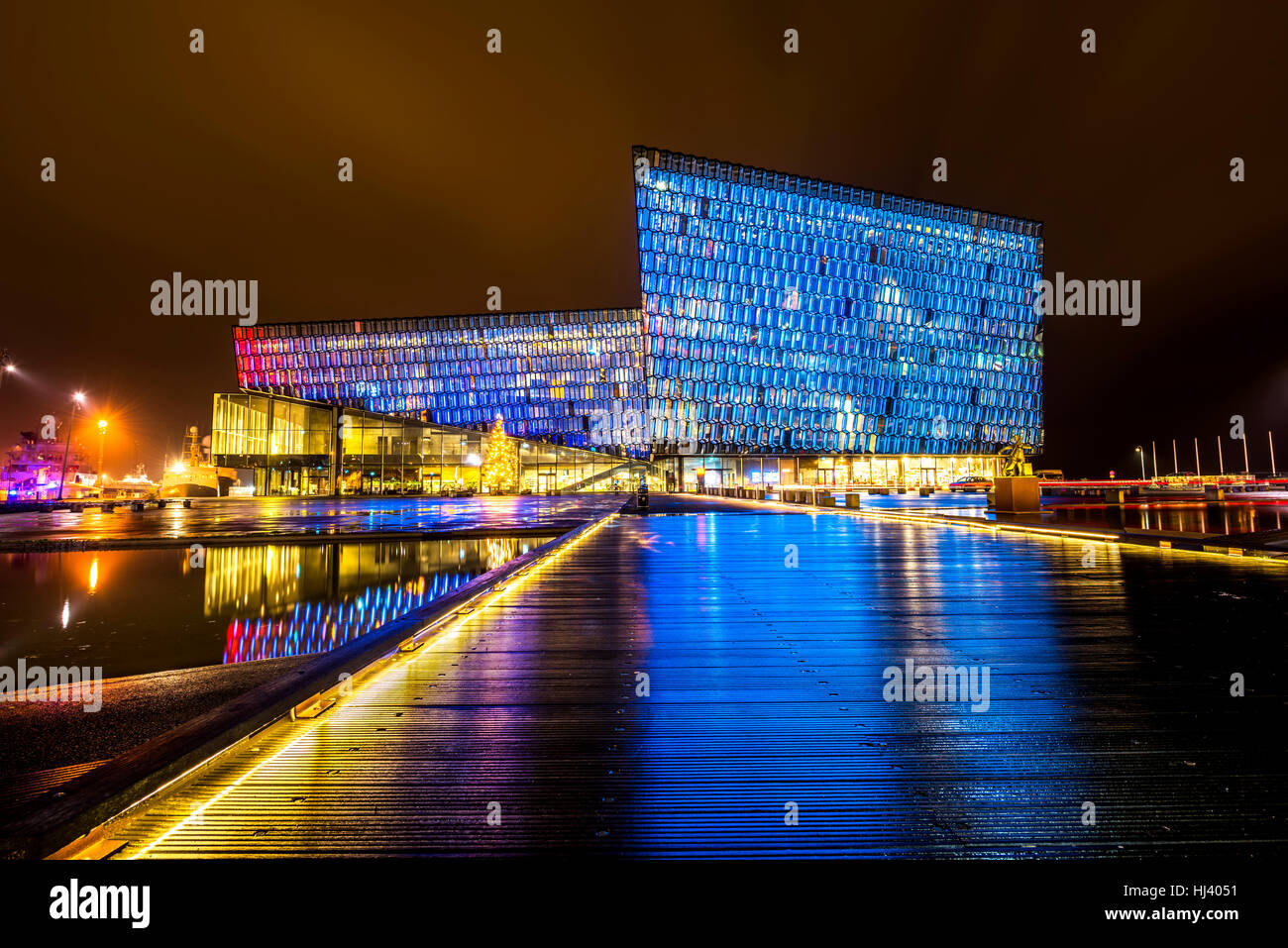 Harpa concert hall in Iceland at night lights up in multiple colors, reflecting on a pool at the front of the building. Stock Photo