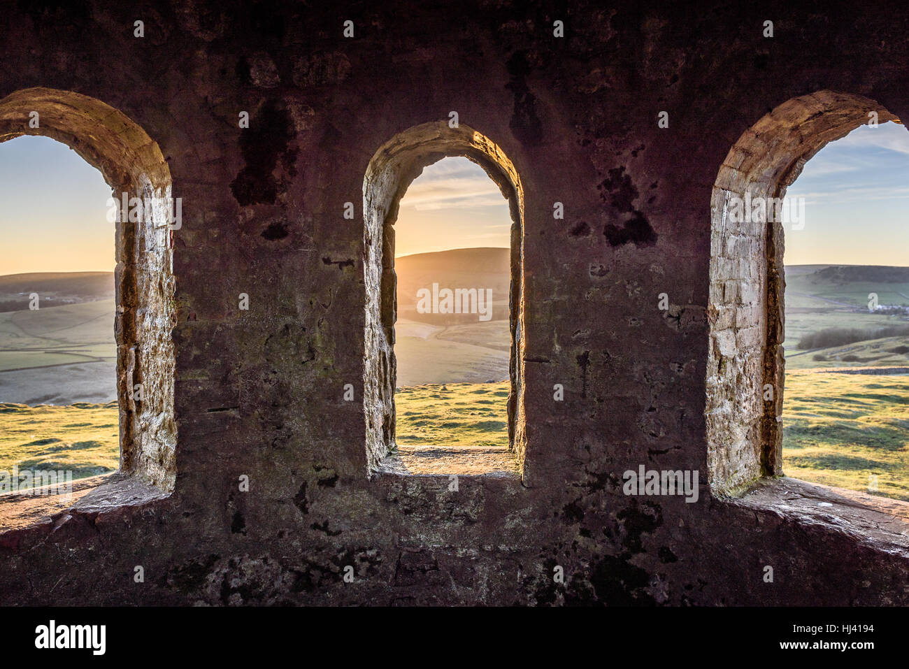 Ancient arch windows in a castle with scenic hills at sunset Stock Photo