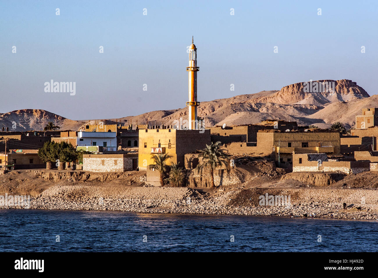 A village along the Nile River in Egypt with the minaret against the mountains at sunset Stock Photo