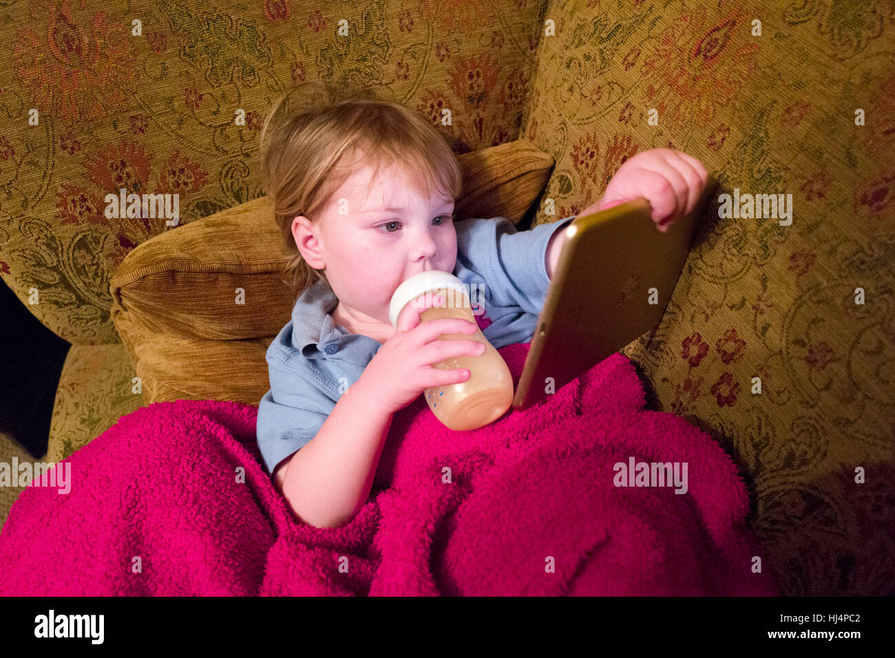 A two year old toddler drinking a bottle of baby milk, while sitting,  lying, on a settee playing on her iPad Stock Photo - Alamy