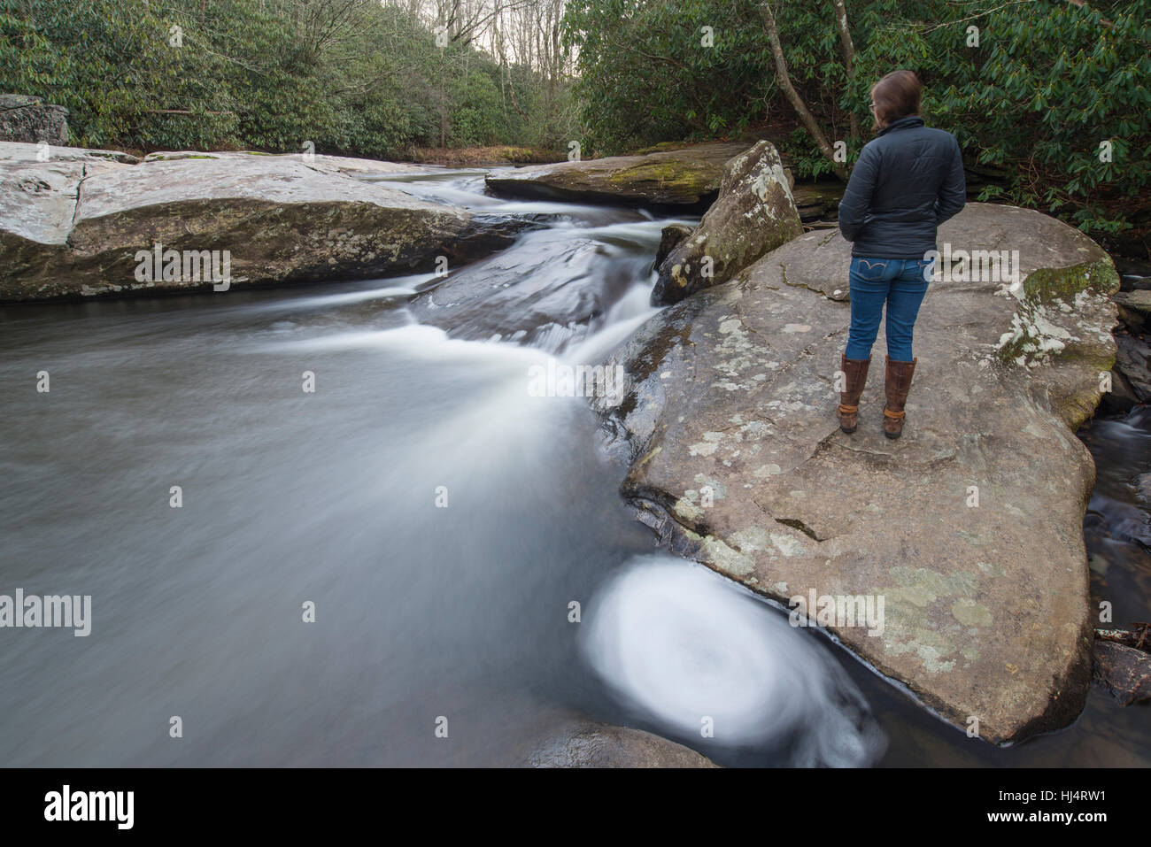 Young woman stands on a rock overlooking mountain stream and waterfall ...