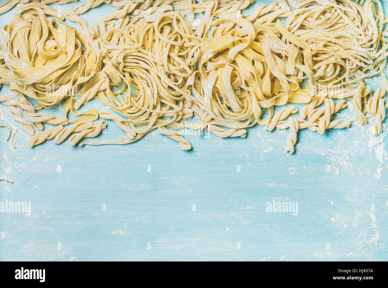 Various homemade uncooked Italian pasta with flour on blue background ...