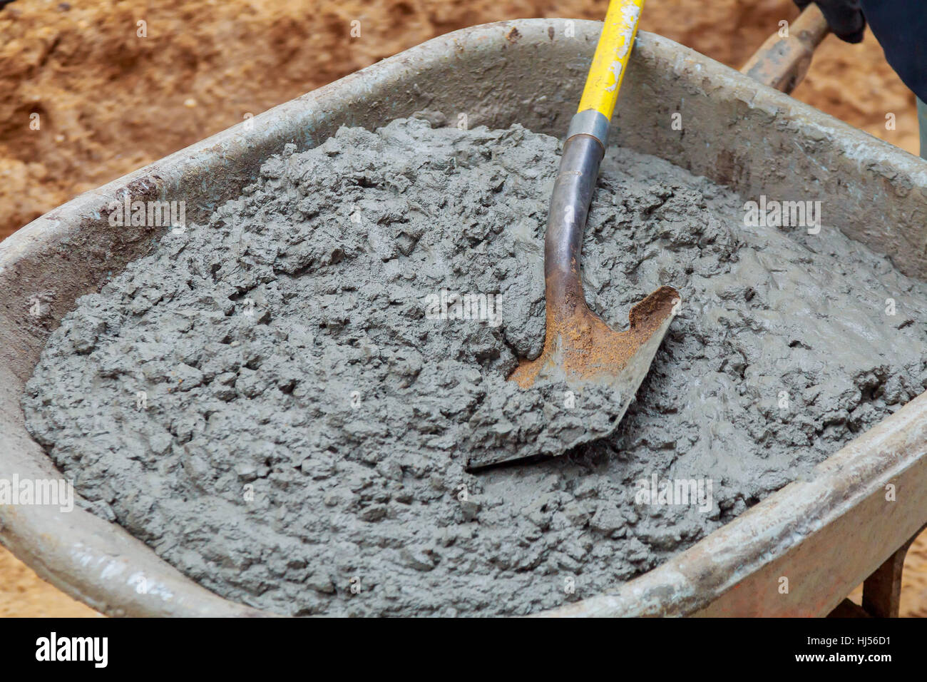 Worker shovels a wet mix of concrete from a wheelbarrow at curb block