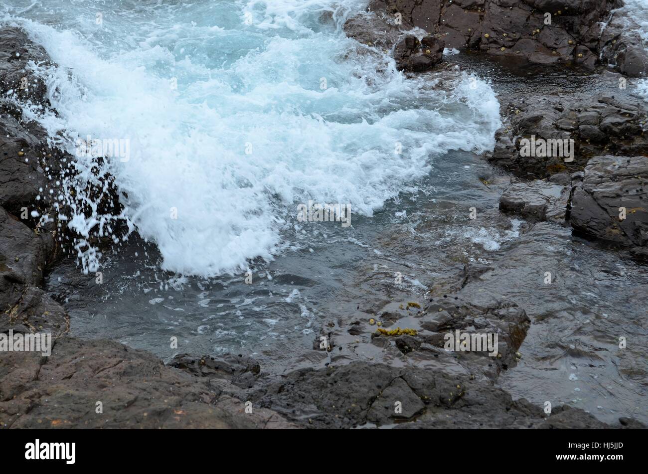 Wave crashing onto rocks flowing into rock pool Stock Photo