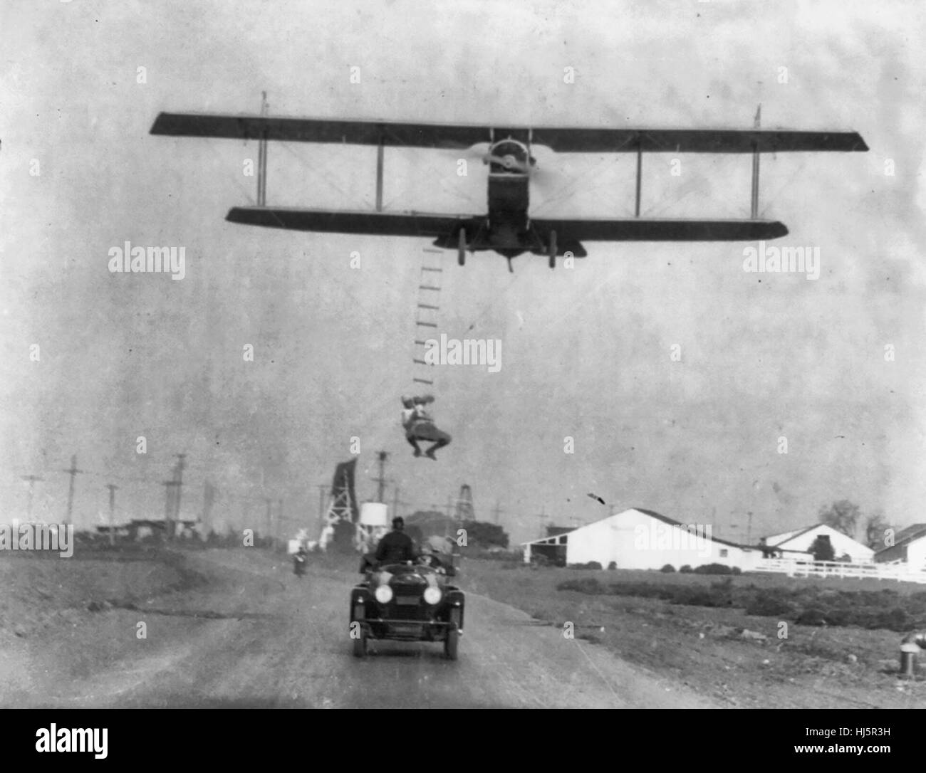 'Fearless Freddie', a Hollywood stunt man, clinging to a rope ladder slung from a plane flown by A.M. Maltrup, about to drop into automobile below: automobile shown. 1921 Stock Photo