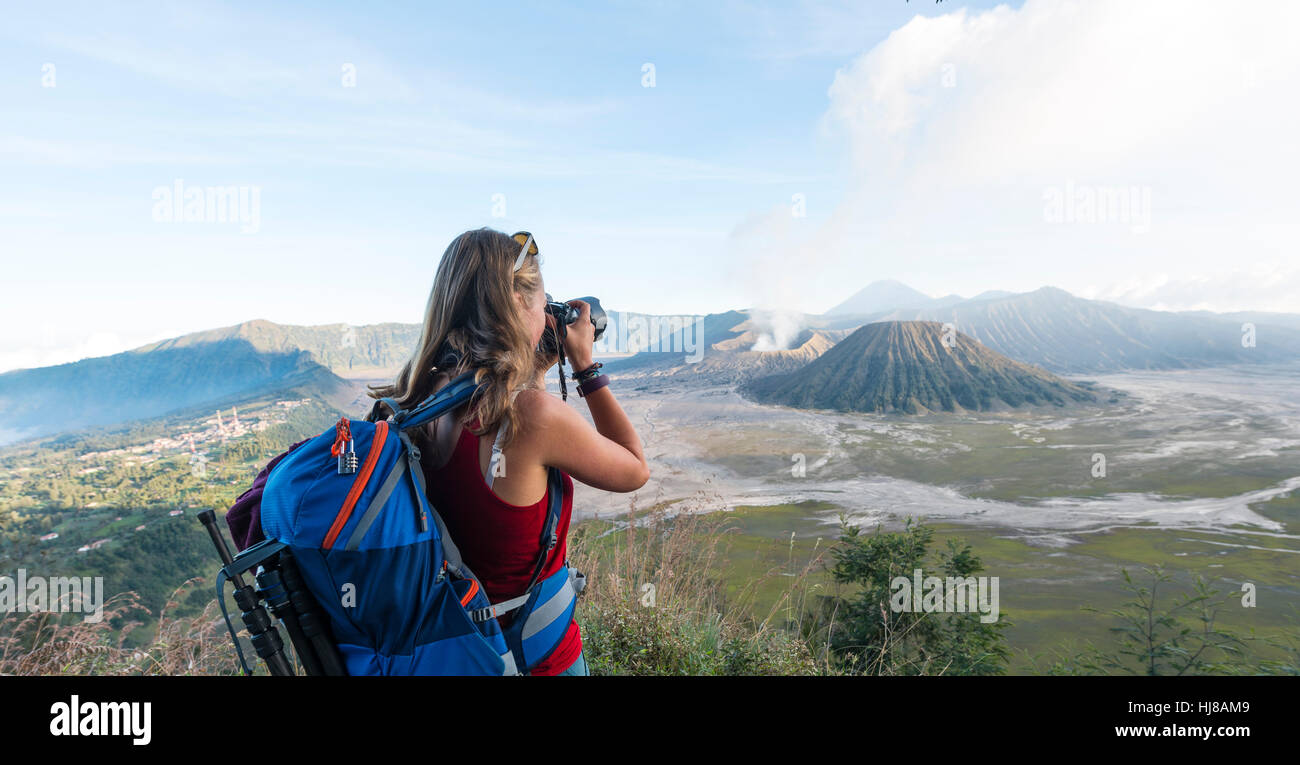 Tourist with camera, smoking volcano Gunung Bromo, Mt. Batok at front, Mt. Kursi at back, Mt. Gunung Semeru, Bromo Tengger Stock Photo