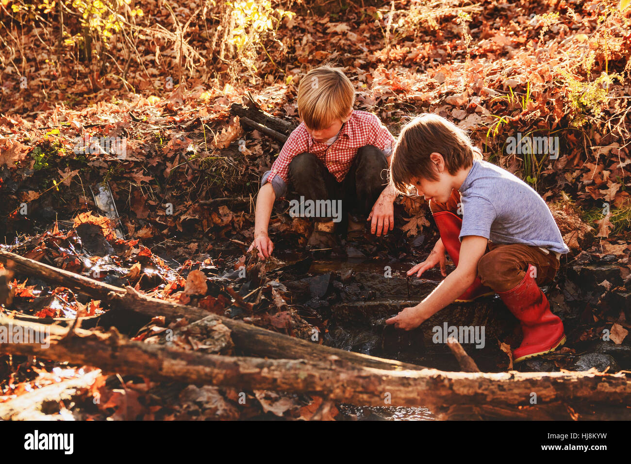 two boys playing in mud by a river Stock Photo