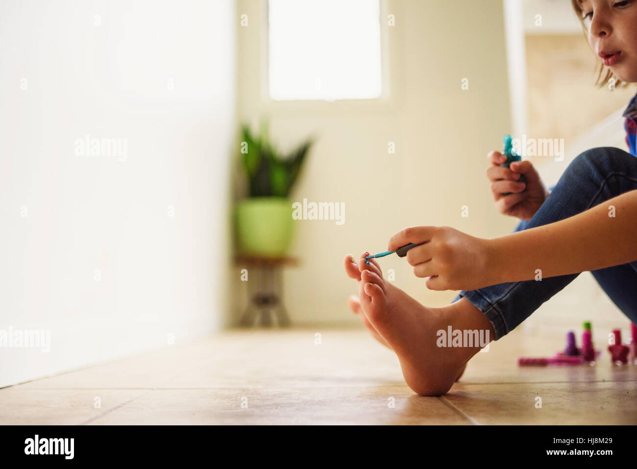 Young girl sitting on the floor painting her toenails with nail varnish Stock Photo
