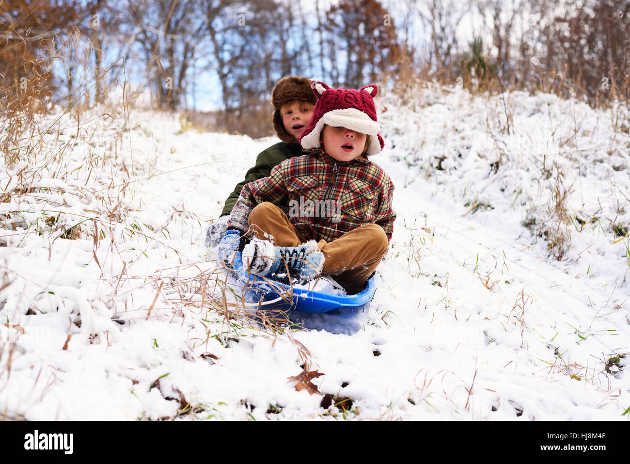 Two children sledding down hill in the snow Stock Photo