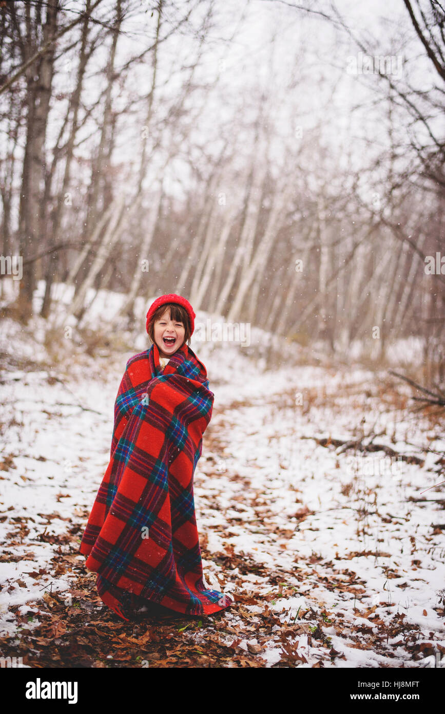 Portrait of a girl wrapped in a blanket standing in the snow laughing Stock Photo