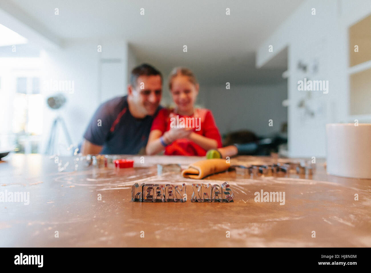 Father and daughter baking with Merry Christmas cookie cutters on table Stock Photo