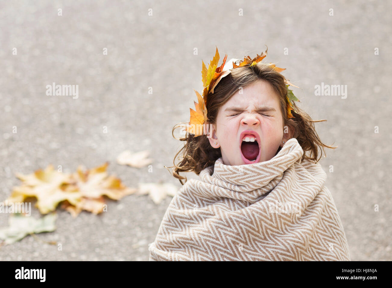 Girl wrapped in a blanket with a wreath of leaves in her hair yawning Stock Photo