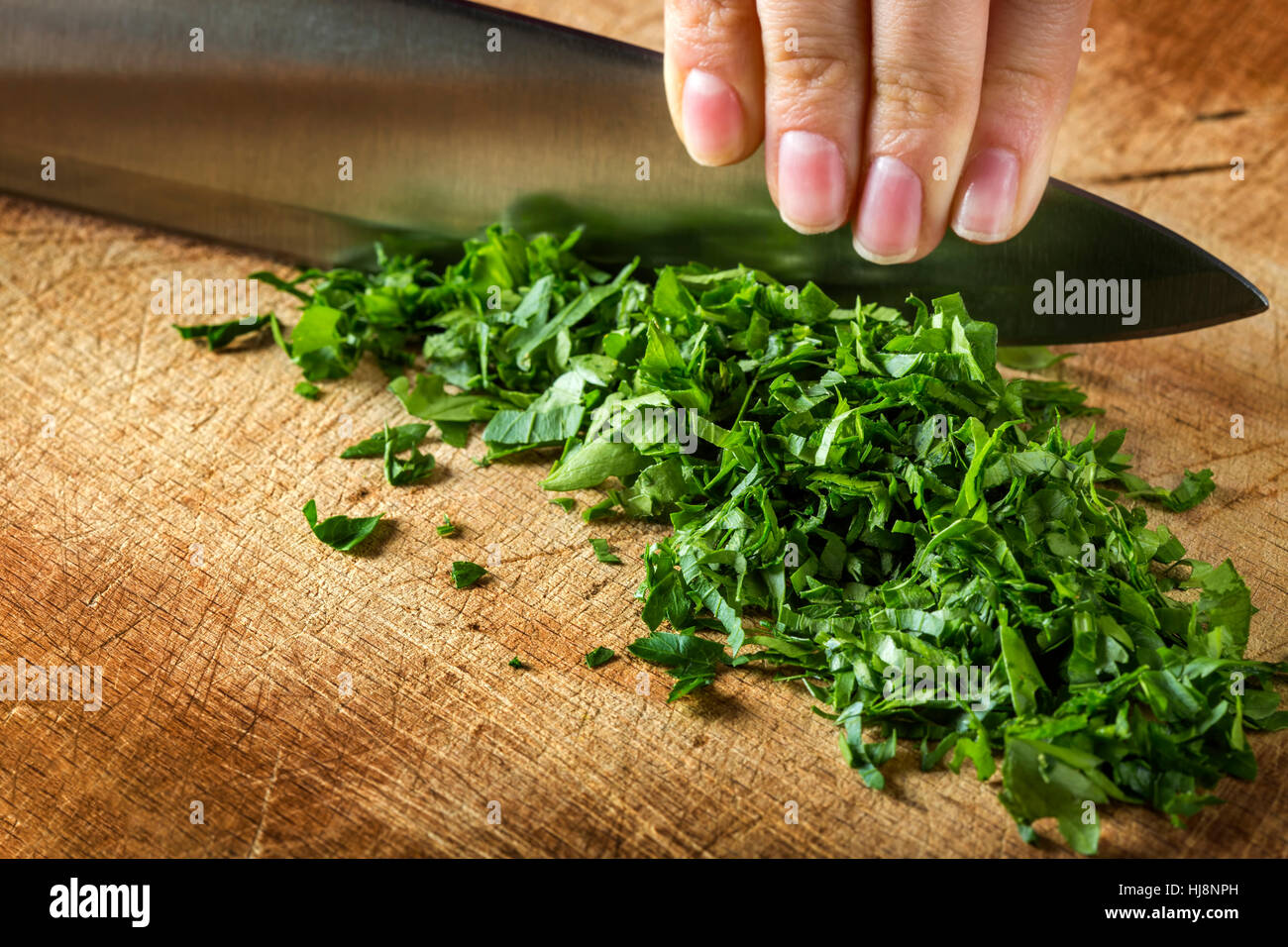 Woman hand cutting raw parsley on wooden cutting board background Stock Photo