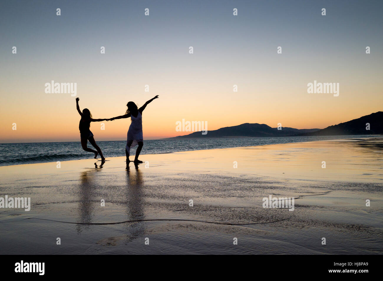 Silhouette of two women on the beach at sunset hi-res stock photography ...