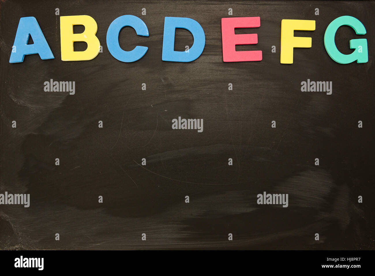 Alphabet stuck on blackboard up to letter g with copy space