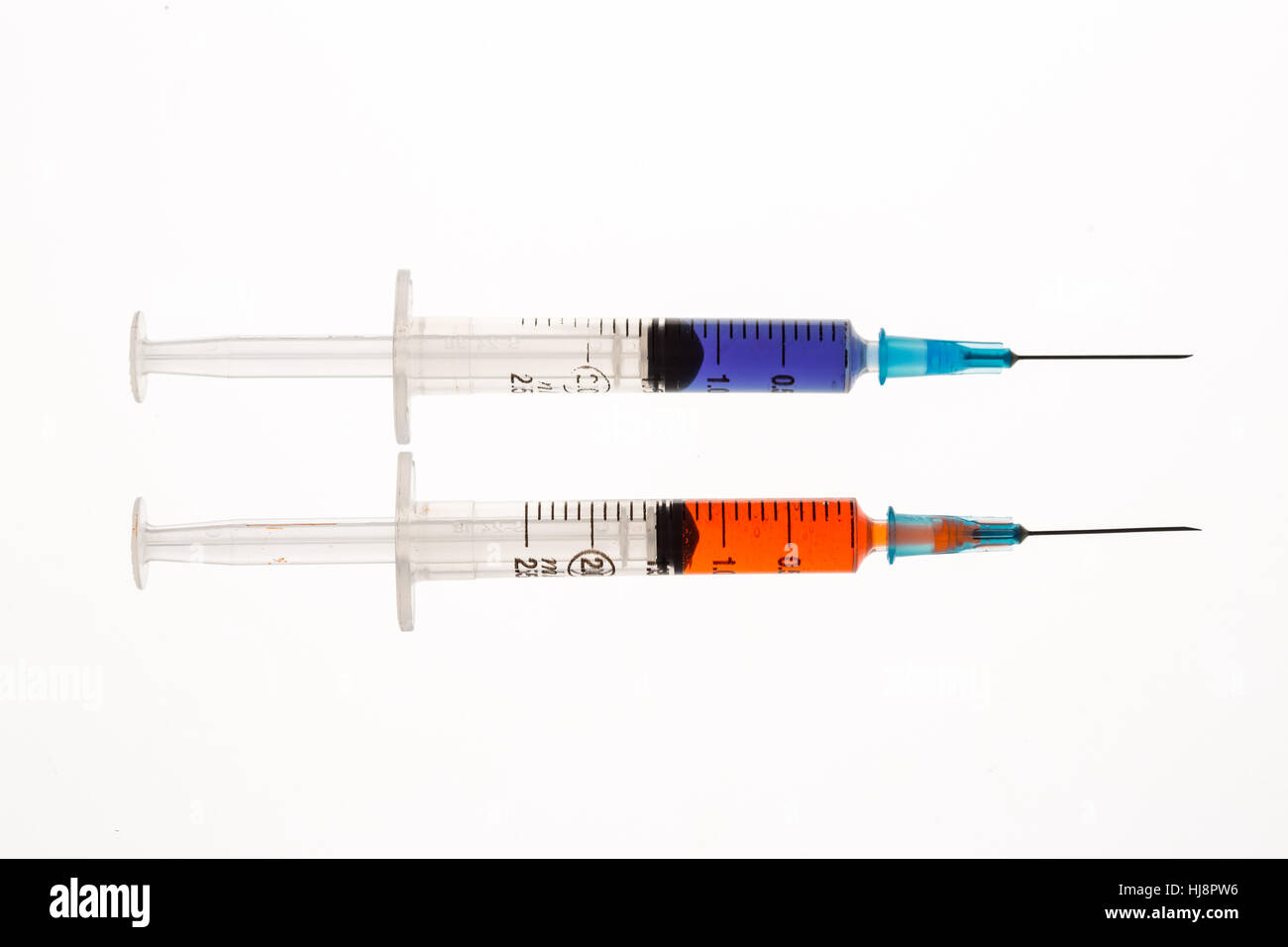 Two syringes holding purple and orange liquid beside each other on white background Stock Photo