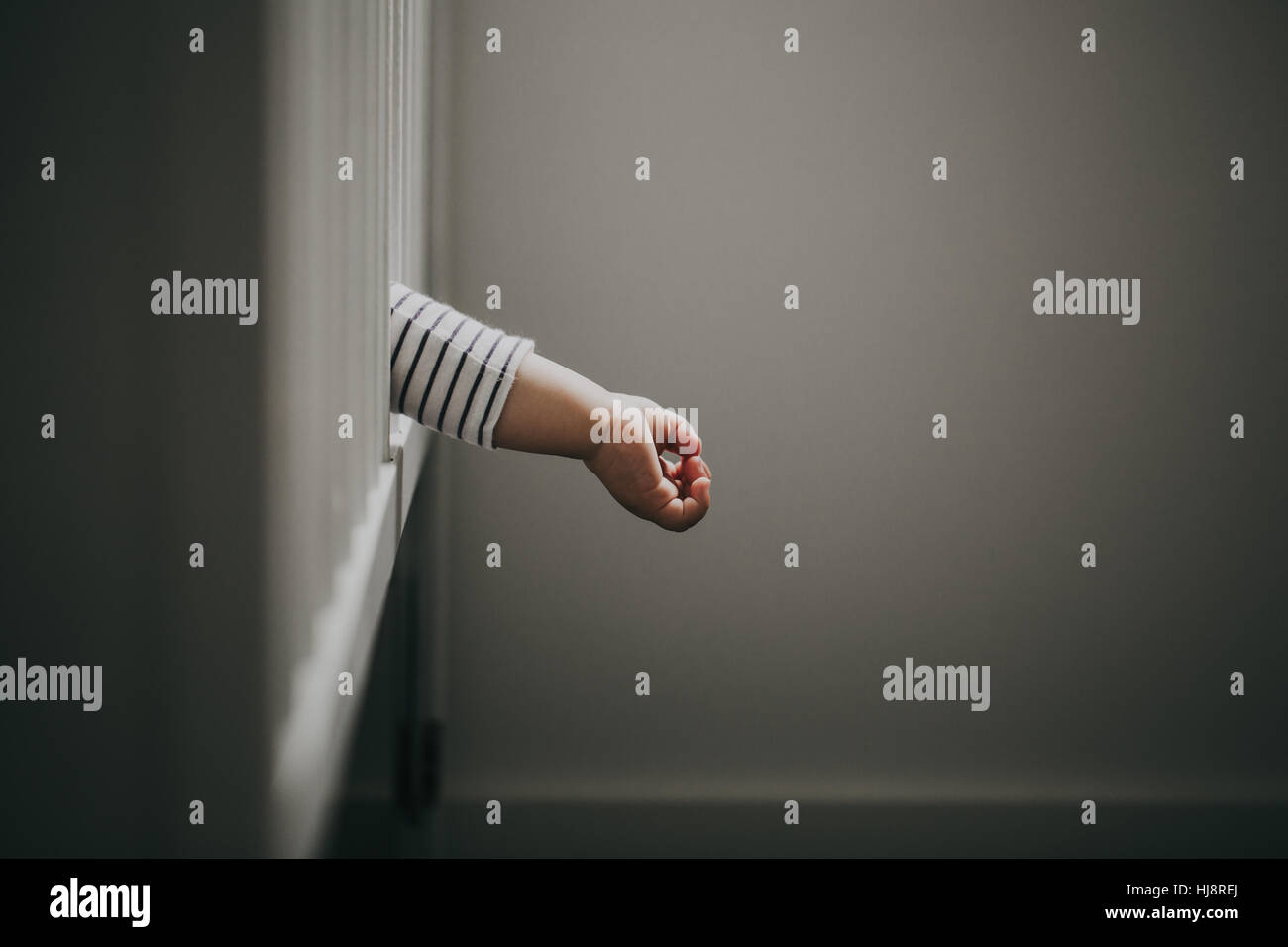 Baby boy's hand hanging out of cot Stock Photo