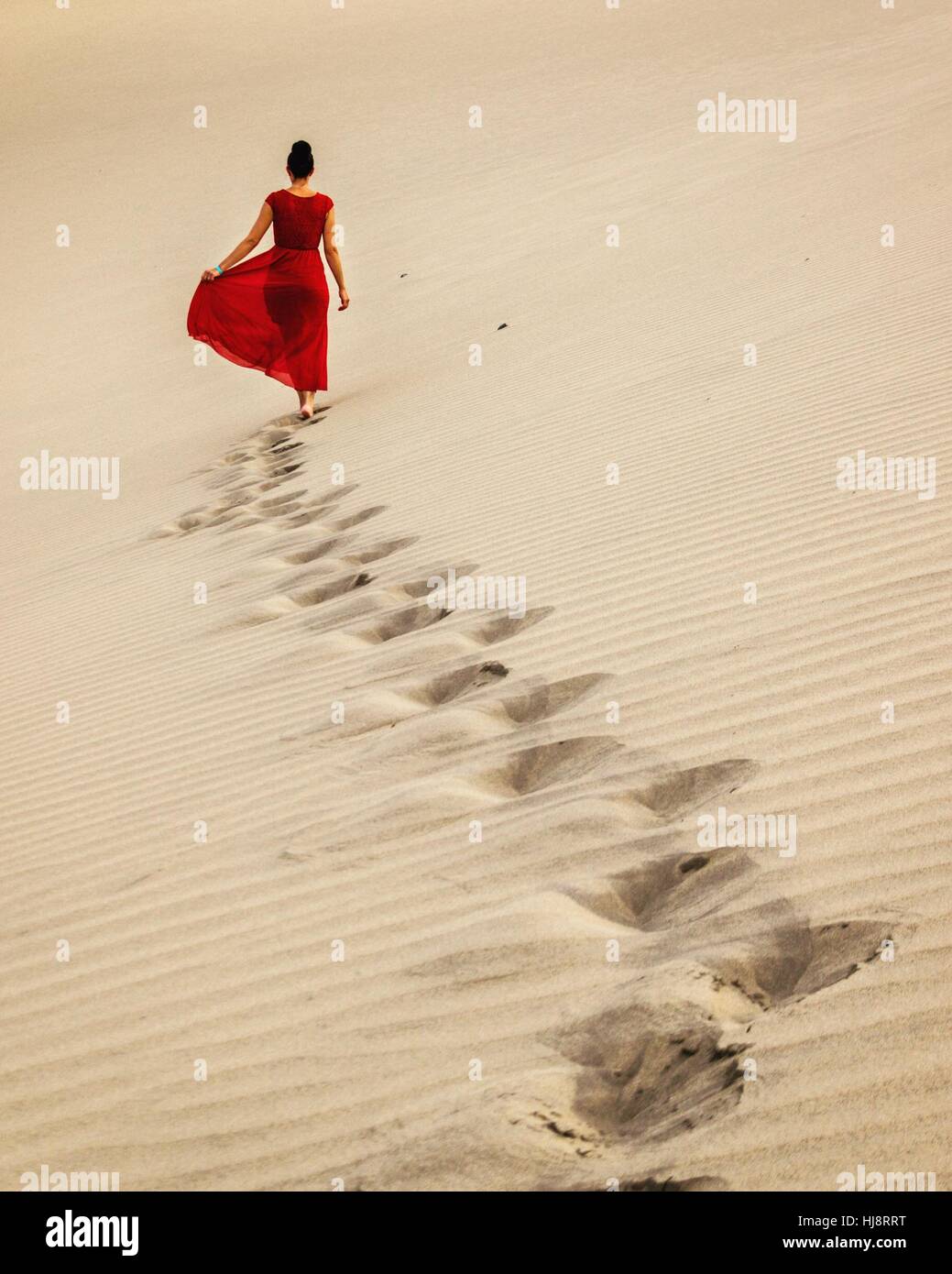 women in red dress walking in the sand, Spain Stock Photo