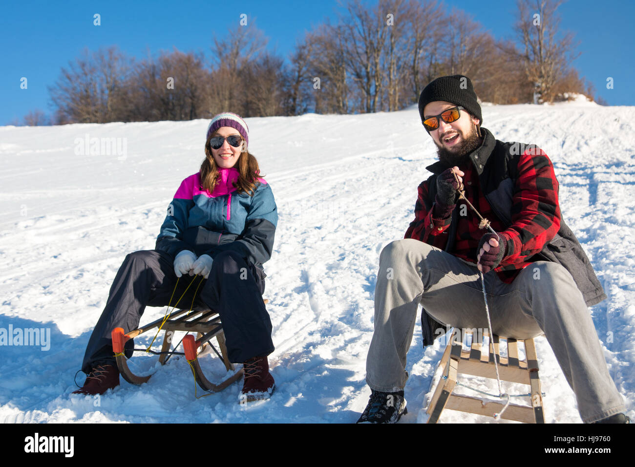 Happy young couple sledding down the hill Stock Photo