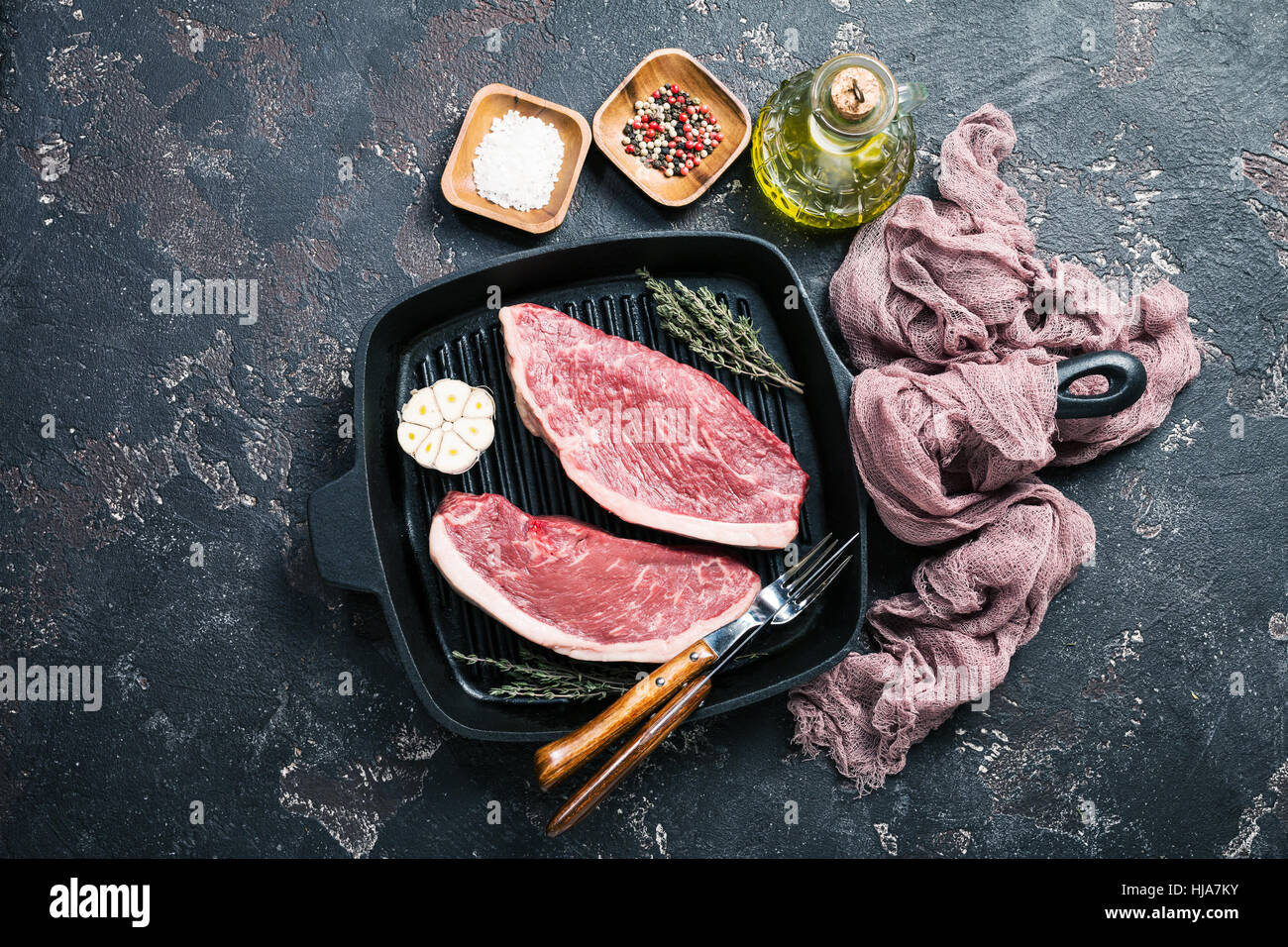 Fresh raw Prime Black Angus beef strip steaks on grill pan over dark rustic concrete background, top view. Ingredients set for making healthy dinner. Stock Photo