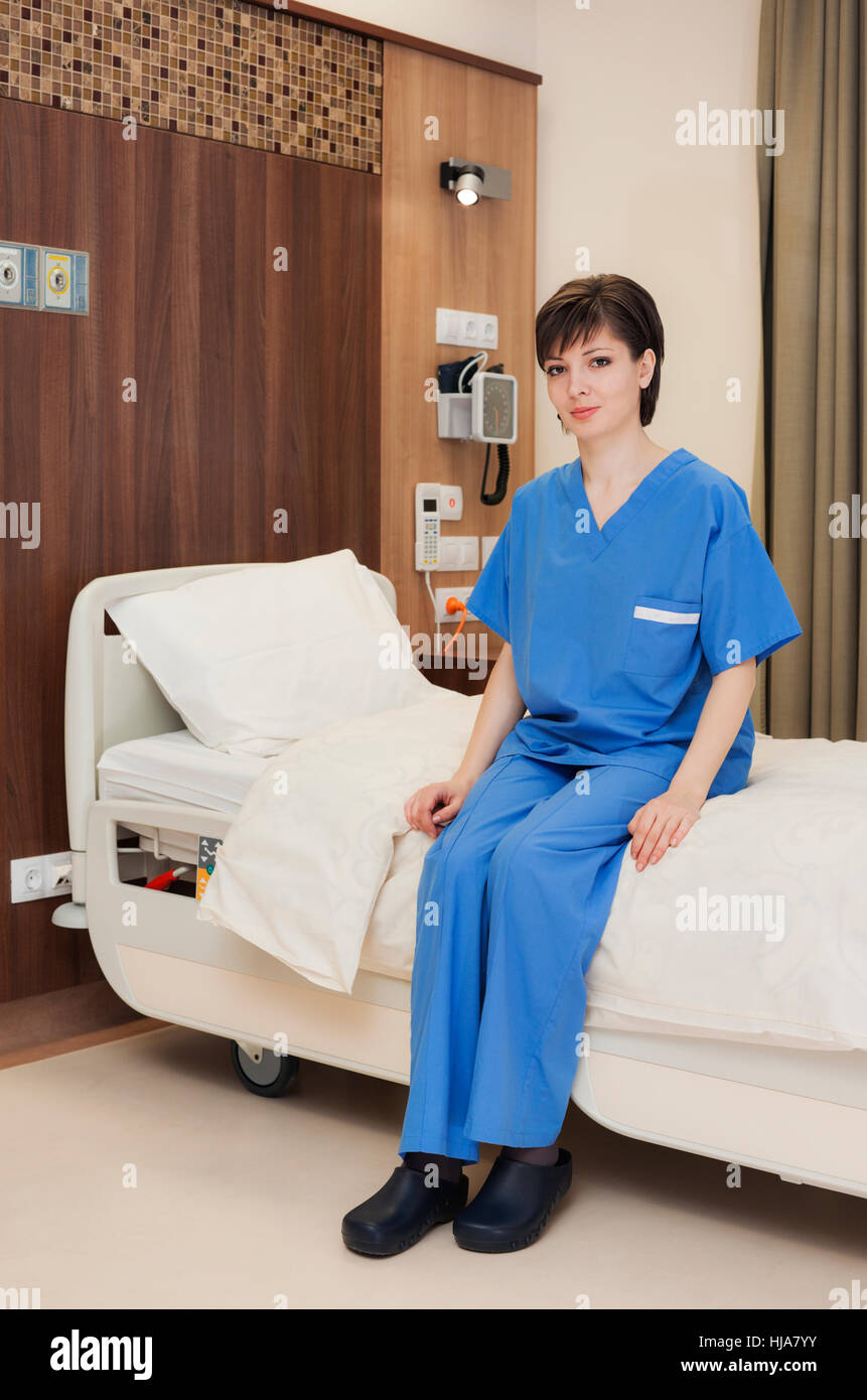 A young female patient sitting on medical bed in modern hospital room. Stock Photo