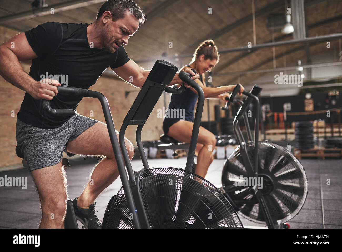 Young man and woman wearing training hardly on cycling machines in