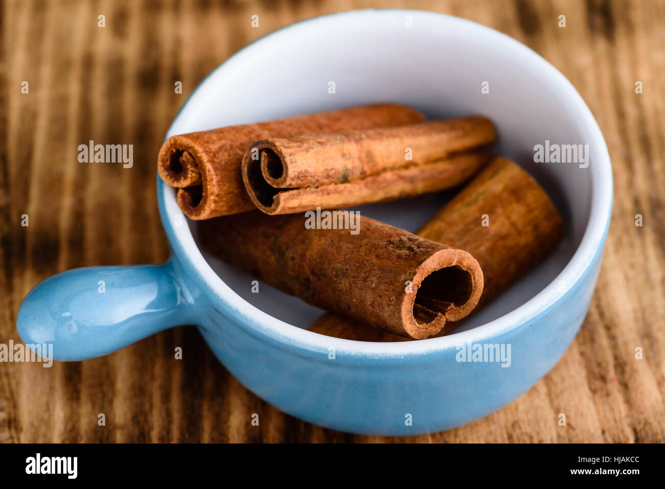 Whole cinnamon inside blue enameled cast iron pot standing om wooden board. Stock Photo