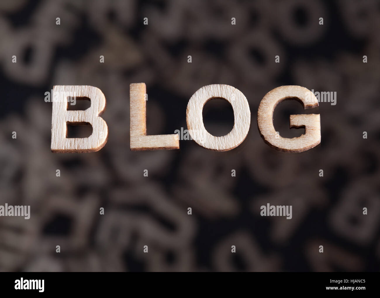 Blog wooden letters text created in wood floating above random letters below out of focus on a black background Stock Photo