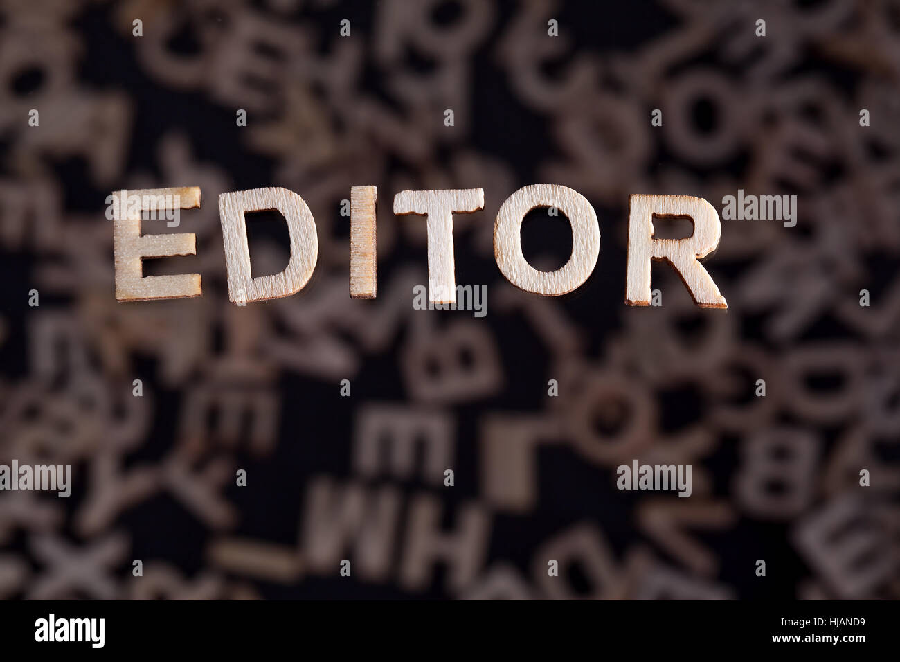 Editor wooden letters created in wood floating above random letters below out of focus on a black background Stock Photo