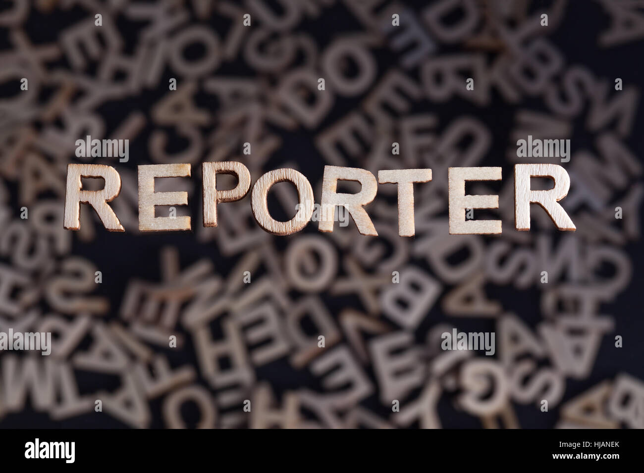 Reporter wooden letters created in wood floating above random letters below out of focus on a black background Stock Photo
