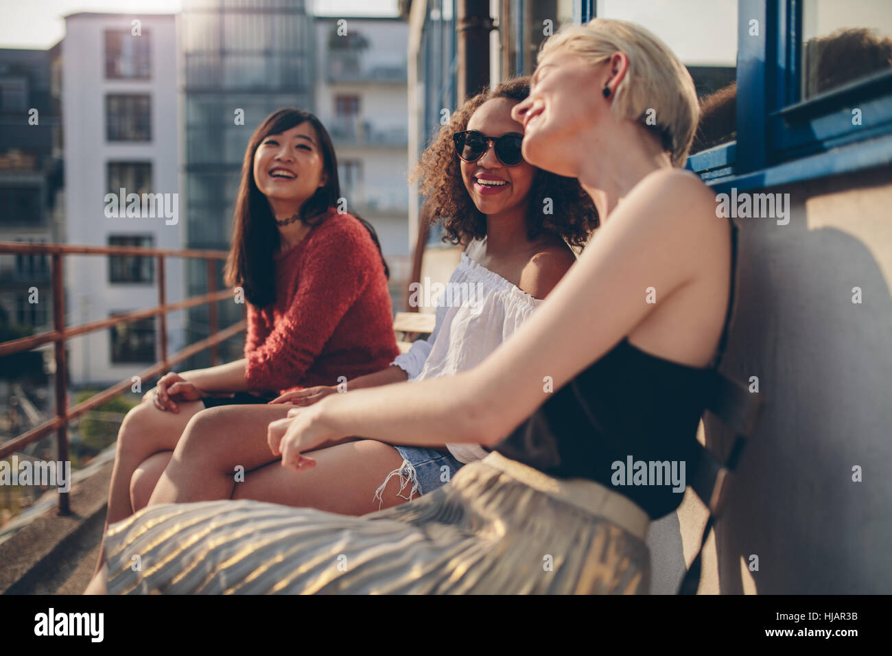 Three young female friends sitting in balcony and having fun. Women relaxing outdoors and chatting. Stock Photo