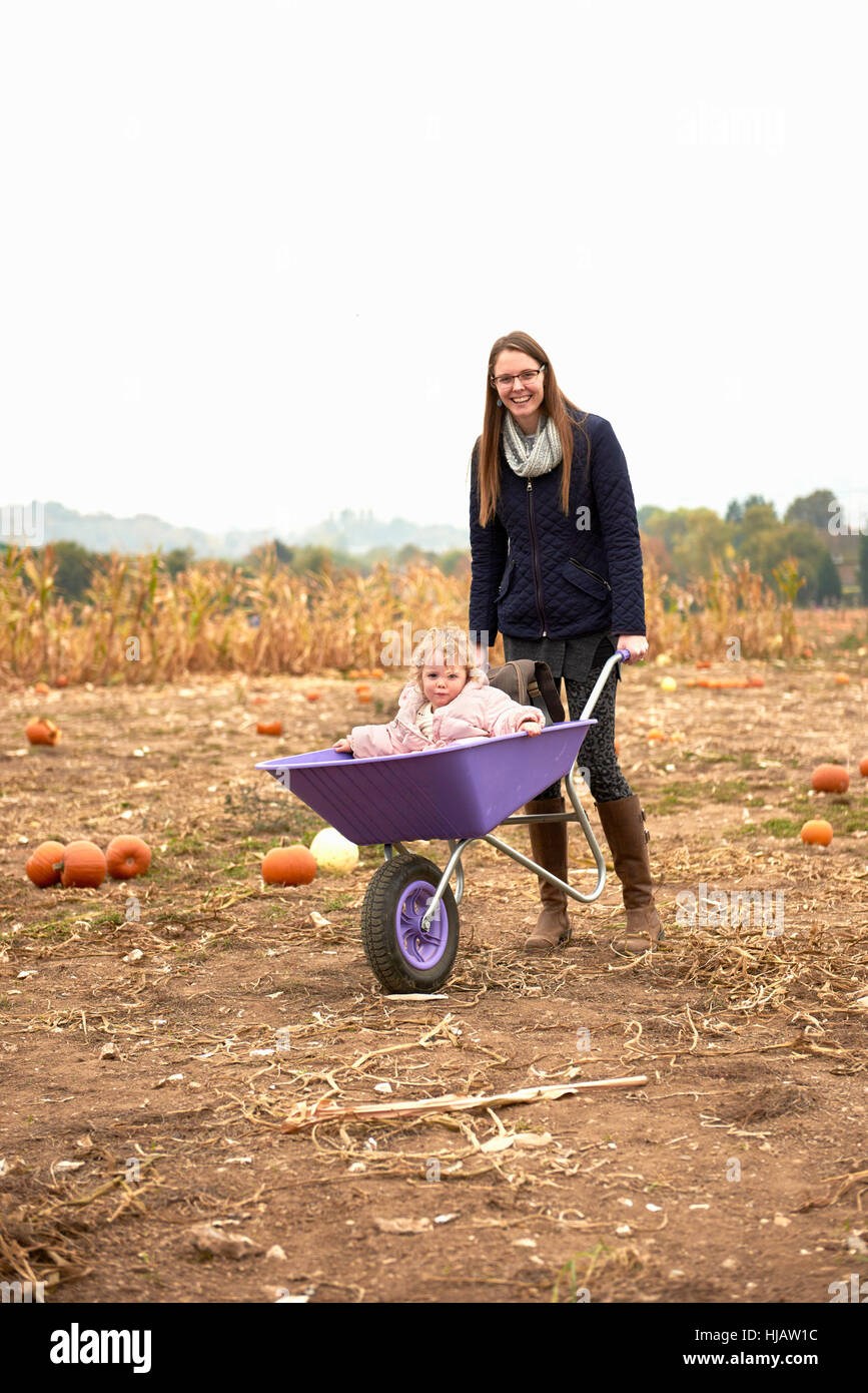 Portrait of mid adult woman pushing toddler daughter in wheelbarrow in ...