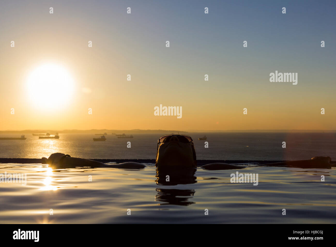 Woman in the swimming pool, with the Todos os Santos Bay and sunset in the background Stock Photo